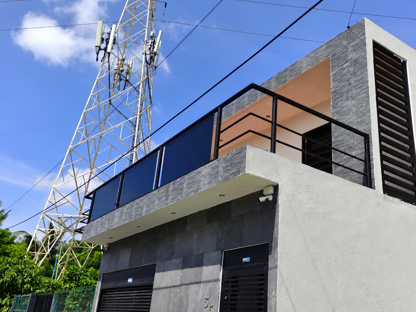 Barandal exterior con cristal azul y herrería negra en fachada residencial